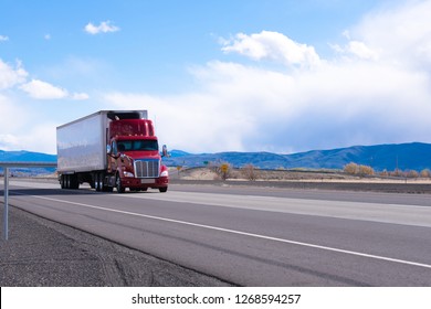 Big rig American bonnet powerful red semi truck with refrigerated semi trailer with refrigerator unit for cooling trailer inside space transporting commercial cargo on flat road in Utah