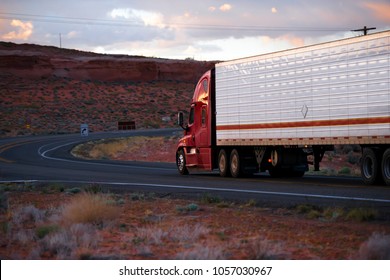 Big Rig American Modern Red Semi Truck Fleet With Refrigerator Semi Trailer Going On Winding Road With Red Rocks Hills Of Arizona Landscape In Twilight With Sunlight Clouds