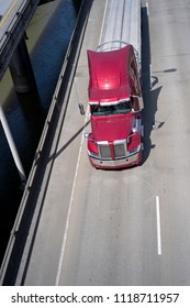 Big Rig American Semi Truck Transporting Empty Flat Bed Semi Trailer To Warehouse Destination For Loading Commercial Cargo By Separated Overpass Road Intersection Along The River With Support Pillars