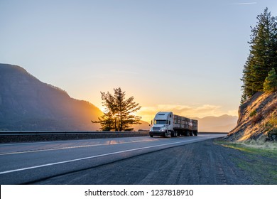 Big Rig American White Long Haul Powerful Semi Truck Transporting Boxes With Fruits On Flat Bed Semi Trailer On Straight Evening Road With Scenic Sunset In Columbia River Gorge