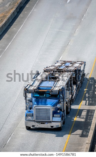 Big rig classic powerful blue bonnet car hauler\
semi truck with empty two levels semi trailer running on the wide\
highway road to dealer warehouse parking lot for loading cars for\
next delivery