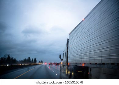 Big Rig Commercial Haul Bonnet Semi Truck Transporting Frozen Cargo In Refrigerator Semi Trailer Driving On The Raining Night Highway With Reflection Lights