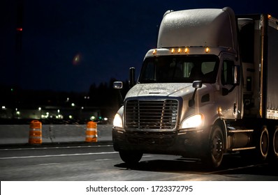 Big Rig Day Cab Heavy-duty Diesel Semi Truck With Roof Spoiler Transporting Commercial Cargo In Semi Trailer Running On The Wet Raining Highway Road At Dark Night Time With Turned On Headlight