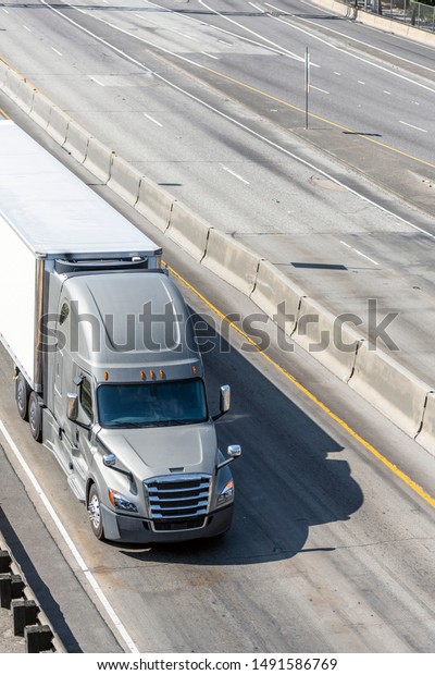 Big rig gray long haul bonnet professional heavy-duty\
semi truck transporting commercial cargo in dry van semi trailer\
for delivery driving on the left line of wide multiline highway in\
sunny day