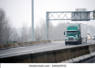 Big Rig Green American Semi Truck With Dry Van Semi Trailer Driving On Winter Slipper Road With Snowy Storm Weather Delivering Commercial Cargo To Point Of Destination