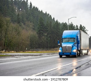 Big Rig Industrial Blue Semi Truck With Turned On Headlights Transporting Cargo In Dry Van Semi Trailer Running On The Night Dark Twilight Wet Road With Reflection On Surface In Rain Weather 