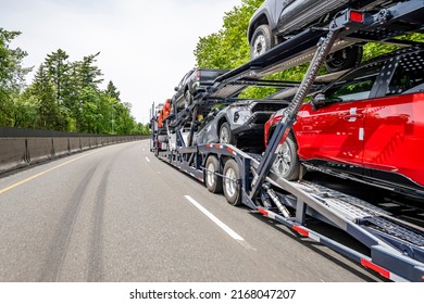 Big rig industrial grade car hauler semi truck tractor transporting vehicles on the modular hydraulic two level semi trailer running on the wide turning divided highway road with trees on the side