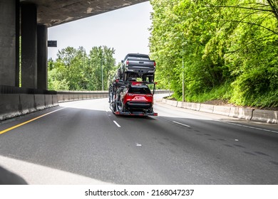 Big rig industrial grade car hauler semi truck tractor transporting vehicles on the modular hydraulic two level semi trailer running under the bridge on the wide turning highway road with trees