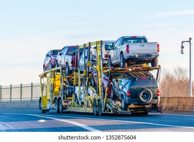 Big rig industrial grade yellow classic bonnet car hauler semi truck transporting cars on two levels semi trailer driving on the overpass road with protective fence on the side