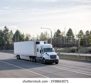 Big rig industrial low cab white semi truck tractor transporting commercial cargo in refrigerated semi trailer with refrigerator unit on the wall running for delivery on the wide divided highway road