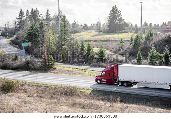 Big rig industrial red American semi truck\
tractor transporting frozen commercial cargo in refrigerated semi\
trailer running for delivery on the wide highway road with with\
exit fork intersection