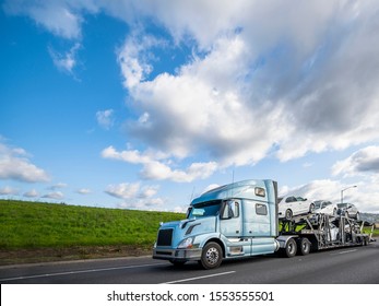 Big Rig Light Blue Long Haulage Car Hauler Semi Truck With Drivers Rest Compartment Transporting Different Cars On The Special Two Levels Modular Semi Trailer Driving On The Flat Road With Green Hill