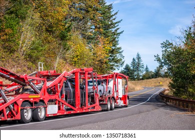Big rig long haul car hauler powerful semi truck transporting different cars on red two levels semi trailer running on winding autumn road with trees on the hillside