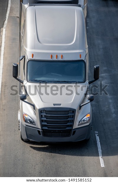 Big rig long haul gray semi truck transporting\
frozen food in refrigerated semi trailer with refrigerator unit on\
the front wall running on the wide interstate highway road with\
safety block