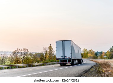 Big Rig Powerful Bonnet American Long Haul Semi Truck Transporting Commercial Goods In Dry Van Semi Trailer Running On The Curvy Winding Evening Road With Autumn Trees