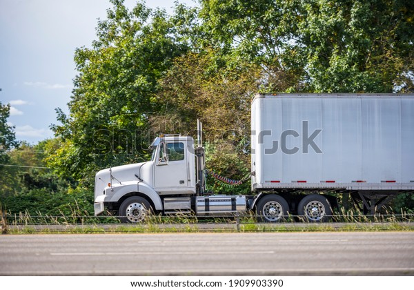 Big rig powerful white commercial haul\
industrial semi truck tractor with day cab for local freight\
transporting cargo in dry van semi trailer driving on the highway\
road for timely delivery