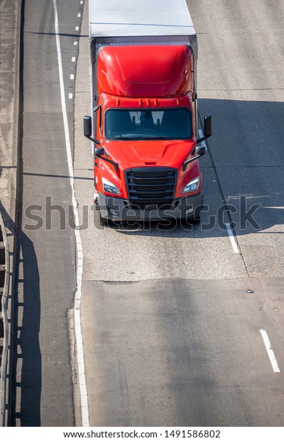 Big rig red long haul bonnet professional heavy-duty\
semi truck transporting commercial cargo in dry van semi trailer\
for delivery driving on the left line of wide multiline highway in\
sunny day