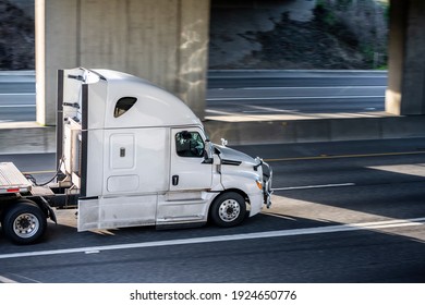 Big rig shiny white semi truck tractor with long cab and auxiliary equipment on the back wall transporting flat bed semi trailer driving on the highway road under the concrete bridge - Shutterstock ID 1924650776
