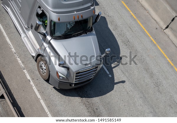 Big rig silver long haul bonnet professional\
heavy-duty semi truck transporting commercial cargo in dry van semi\
trailer for delivery driving on the left line of wide multiline\
highway in sunny day