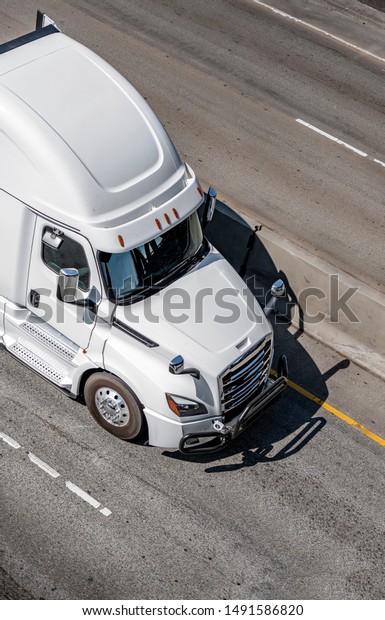 Big rig white bonnet semi truck tractor with grille\
guard driving on the wide multiline highway road with road marking\
running to warehouse for pick up loaded semi trailer for the next\
delivery trip