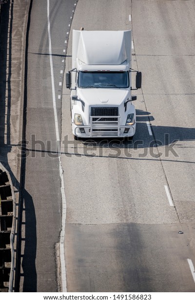 Big rig white bonnet semi truck tractor with grille
guard driving on the wide multiline highway road with road marking
running to warehouse for pick up loaded semi trailer for the next
delivery trip