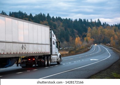 Big rig white long haul semi truck with semi trailer running with turned on headlights on rain dusted wet raining highway driving with another cars traffic in twilight evening time - Shutterstock ID 1428172166