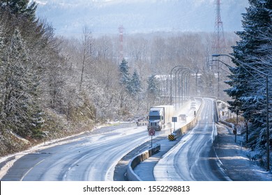 Big rig white long haul semi truck with grille guard transporting commercial goods in dry van semi trailer driving on the turning winter snowy wet dangerous highway with trees on the sides