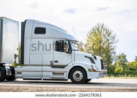 Big rig white long haul industrial semi truck tractor with sleeper cab compartment for truck driver rest transporting cargo in dry van semi trailer driving on the highway road for timely delivery