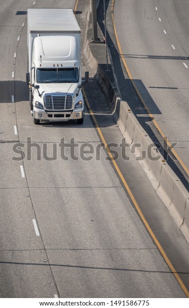 Big rig white long haul bonnet professional\
heavy-duty semi truck transporting commercial cargo in dry van semi\
trailer for delivery driving on the left line of wide multiline\
highway in sunny day