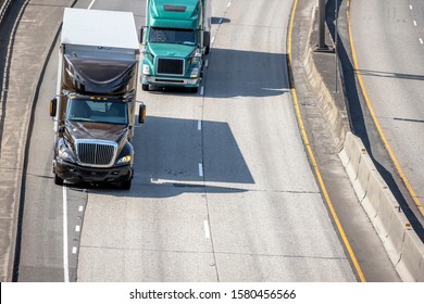 Big rigs classic brown and green bonnet semi trucks transporting commercial industrial cargo in dry van semi trailers driving on merging road lines on wide turning highway