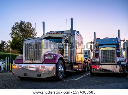 Big rigs classic long haul bonnet American idol semi trucks standing in row on truck stop parking lot at evening time reflecting sunset and all around by a lot of chrome parts mounted on tractors