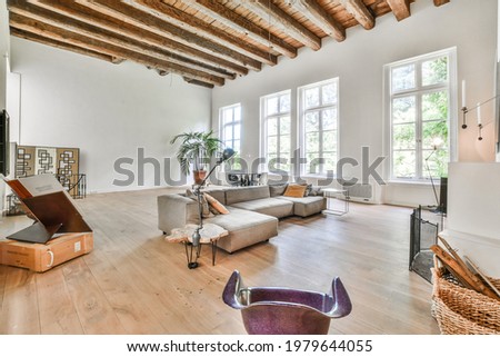Big room with high wood beamed ceilings furnished with gray couch and art design elements in minimalist style