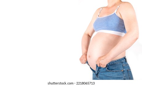 Big Round Belly Grow Of A Young Pregnant Woman No Face In Blue Jeans And Top, Holding Too Small Tight Unfit Trousers Isolated On White Background. Pant Width Open Trying To Fit In Old Clothes, Banner