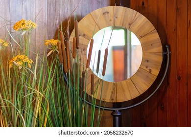 Big Round Mirror, With A Thick Wood Frame Around It Against A Wooden Wall. Decorative Flowers In Interior. 