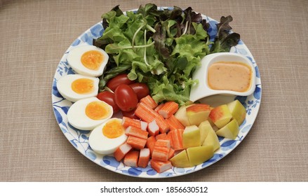 A Big Round Plate With Variety Of Salad Vegetables, Eggs, Crab Stick, Apple And Spicy Dressing Served In Small Sauce Cup