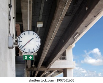big round shape electronics clock and emergency exit sign hanging on concrete wall at stairway to sky train station with blue sky and cloud, analog clock for check time when traveling in the city
