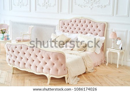 Big royal bed with pillows in elegant bedroom interior, copy space. Honeymoon suite, free space. Female bedroom in pink and white colors. Luxury bed in romantic style bedroom in white room. Boudoir