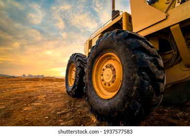 Big rubber wheels of soil grade tractor car earthmoving at road construction side. Close-up of a dirty loader wheel with a large tread with sky sunset