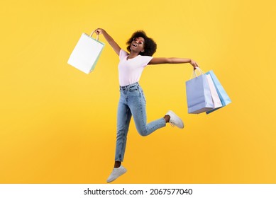 Big sales concept. Young african american lady jumping with colorful shopping bags over yellow background. Joyful black woman enjoying seasonal discounts and black friday