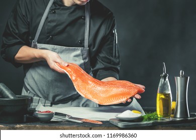 The big salmon is in the hands of the chef cook. He is using a knife to slice salmon fillet 