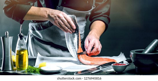 The big salmon is in the hands of the chef cook. He is using a knife to slice salmon fillet  - Powered by Shutterstock