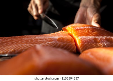 The big salmon is in the hands of the experienced Japanese chef.
He is using a knife to slice salmon fillet for sashimi and sushi.