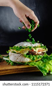 Big Sandwich On Black Background Street Food, Fast Food. Homemade With Beef, Cheese On Wooden Table.  Hand Of Chef Sprinkling With Herbs