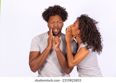 Big secret. Joyful black woman whispering something into her boyfriend's ear, cheerful couple gossiping together on white studio background - Powered by Shutterstock