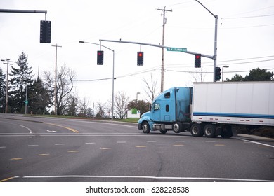 Big Semi Truck With A Trailer For Long Haul At The Turn Of The Road With Traffic Lights Stopped At An Intersection At A Red Traffic Light.