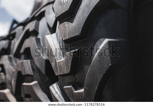 Big  set of black huge big truck, tractor or bulldozer\
loader wheel close-up on stand, shop selling tyres for farming and\
big vehicles Construction machinery. Lot of pattern tread of\
Off-road tires. 
