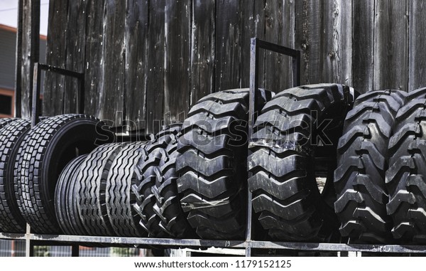 Big  set of black huge big truck, tractor or bulldozer\
loader wheel close-up on stand, shop selling tyres for farming and\
big vehicles Construction machinery. Lot of pattern tread of\
Off-road tires. 