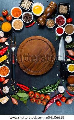 Big set of spices, vegetables,chef's knife, fork for meat and empty wooden round cutting board on a black background