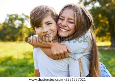 Big sister happily and lovingly hugs little brother in summer in the park