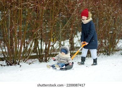 Big Sister And Her Toddler Brother Having Fun Outdoors. Young Girl Playnig With Her Sibling Boy On Winter Day. Kids During Winter Break. Children Exploring Nature Together.